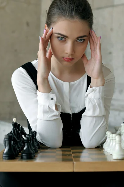 Girl put her hands to her temples before the a chess game. — Stock Photo, Image