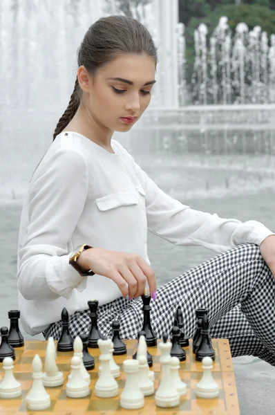 Chica jugando ajedrez sentado cerca de la fuente . —  Fotos de Stock