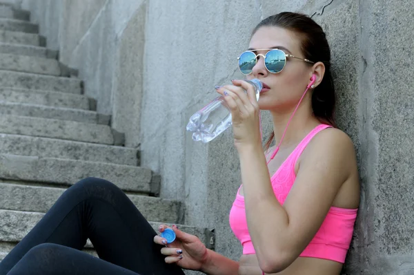 La mujer bebe agua y escucha música — Foto de Stock