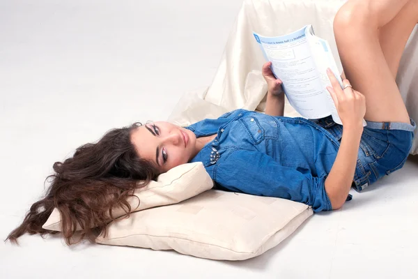 Женщина в синей джинсовой рубашке читает книгу, лежащую на полу — стоковое фото