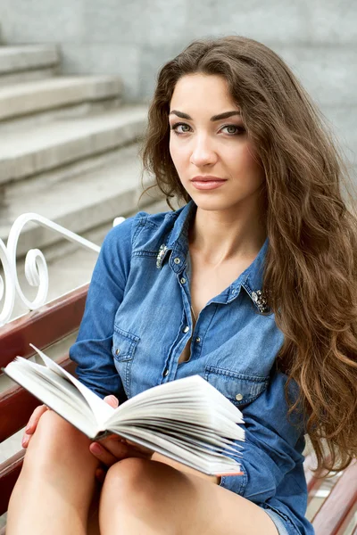 Zwanzig-jähriges Mädchen liest ein Buch, während es auf einer Bank sitzt — Stockfoto