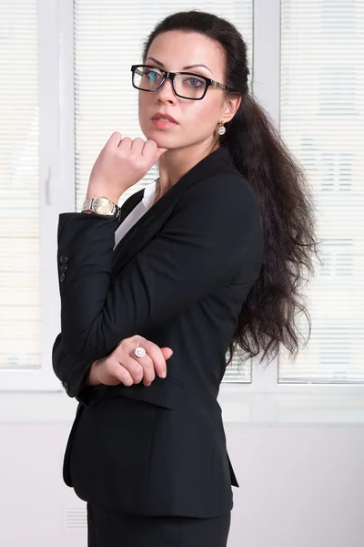 Woman leader in black business suit and glasses standing turned