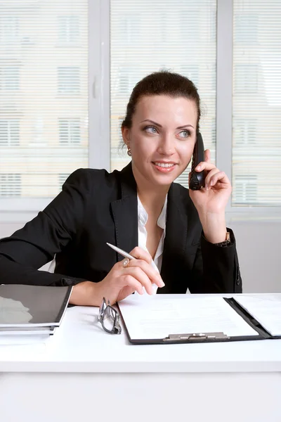 Female signs documents sitting at the table and talking on phone — Stock Photo, Image