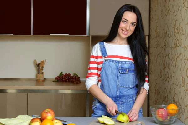 Mavi tulum içinde esmer ev kadını mutfakta bir elma cuts — Stok fotoğraf