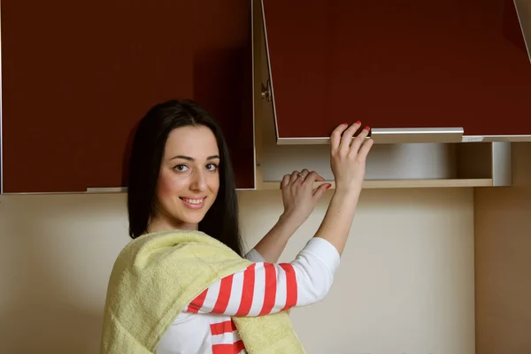 Housewife brunette in home clothes kitchen cupboard opens