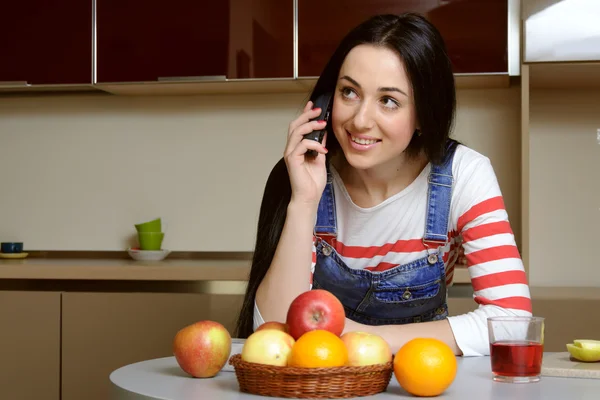 Brünette Hausfrau in blauen Overalls telefoniert lächelnd Stockbild