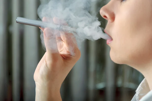 Ragazza fuma una sigaretta elettronica ed espira vapore aromatizzato . — Foto Stock