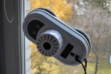 Pencereleri ve seramik fayansları bir pencere ve sonbahar manzarasına karşı temizleyen robot. Akıllı ev aletleri, dışarıdaki ve içerideki pencereleri temizleyen robotlar..