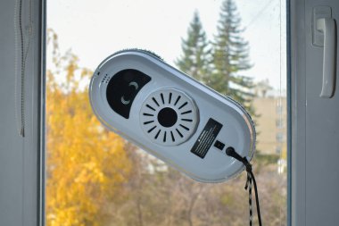 Pencereleri ve seramik fayansları bir pencere ve sonbahar manzarasına karşı temizleyen robot. Akıllı ev aletleri, dışarıdaki ve içerideki pencereleri temizleyen robotlar..
