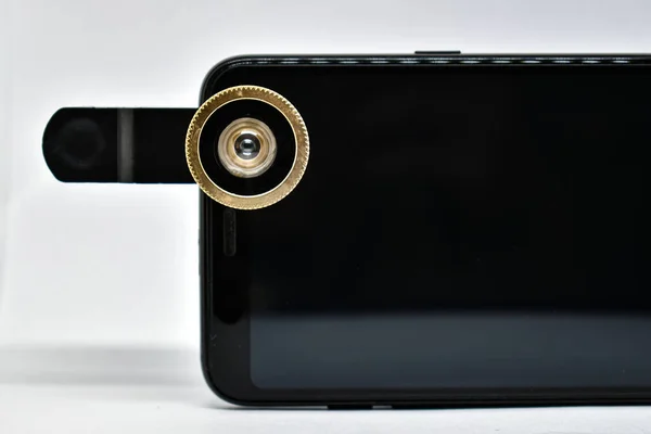Black smartphone with lens on clip isolated on white. An external wide-angle lens and clip are supplied with the mobile phone. A modern smartphone with an extra lens. Close-up