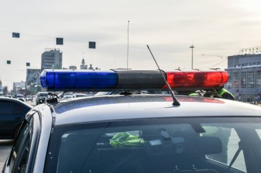 Şehir manzarasına karşı polis arabasındaki işaret lambaları. Polis arabasının çatısında mavi ve kırmızı ışıklar yanıp sönüyor. Bir suçluyu durdurmak, trafik kurallarını çiğnemek..