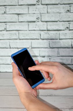 Tuğla duvarın yanında boş ekranlı cep telefonu tutan bir adam. Eller akıllı telefonu arka planda tutar, fotokopi aletiyle taklit eder. Tasarım için boş ekranlı telefon. İnternetten alışveriş, blog yazma