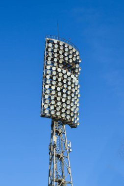 Stadyumdaki spot ışıkları mavi yaz gökyüzüne karşı. Spor salonu ya da stadyum için yüksek metal aydınlatma kulesi. Dibe vurun. Stadyum ışıkları yansıtıcı ve koyu mavi gökyüzü