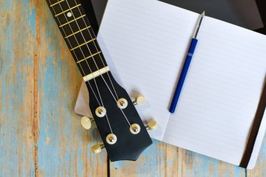 ukulele fretboard ve ahşap masa üzerinde not defteri, metin için yer. Hawaii gitarı çalmayı çevrimiçi öğrenme. Ukulele, dizüstü bilgisayarın yanında ahşap bir arka planda. seçici odak