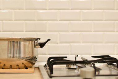 Paslanmaz çelik tencere beyaz tuğla mutfak duvarına karşı gaz ocağının yanında duruyor. Mutfak içi gaz sobası ve çatal bıçaklarla dolu. Mutfak eşyaları. Yemek pişirmek için çalışma alanı. Mutfak eşyaları. Metin için boşluk