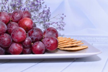 Tabakta üzüm ve kraker var. Şarabın yanında atıştırmalık bir hayat. Kırmızı üzümler açık arkaplanda bej tabakta. Beyaz arka planda peynirli kraker olan tatlı üzümler, metin için yer