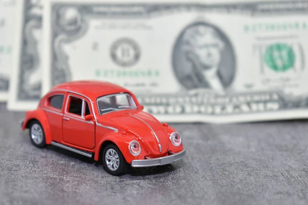 miniature red car on the background of us dollars banknotes. Red toy car and money on gray background. Savings concept, car loan, gasoline prices and car insurance