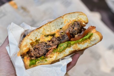 Lezzetli hamburgerler insanın elinde. Hamburger tutan erkek eli, yakın plan. Fast food, sağlıksız yemek. Evde nefis çizburger yiyen bir adam. Yemek teslimatı.