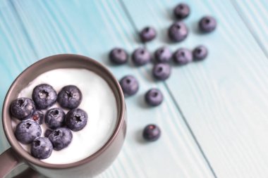 Mavi panoların arka planında yoğurt ve yabanmersinli bir fincan. Lezzetli süt yoğurdu ve ahşap masanın üstünde dağınık böğürtlen. sağlıklı diyet yemekleri. Mesaj için yer var. Yukarıdan bak. Düz yatıyordu.