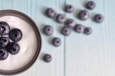 Mavi panoların arka planında yoğurt ve yabanmersinli bir fincan. Lezzetli süt yoğurdu ve ahşap masanın üstünde dağınık böğürtlen. sağlıklı diyet yemekleri. Mesaj için yer var. Yukarıdan bak. Düz yatıyordu.