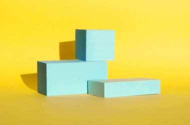 Minimalist soyut arka plan. Sarı arka planda açık mavi renkli üç boyutlu geometrik şekiller. Modern tarz, ürün podyumları, sanat. Seçici odak, metin için alan