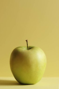Sarı yatay arka planda tek yeşil elma. Minimalizm kavramı.