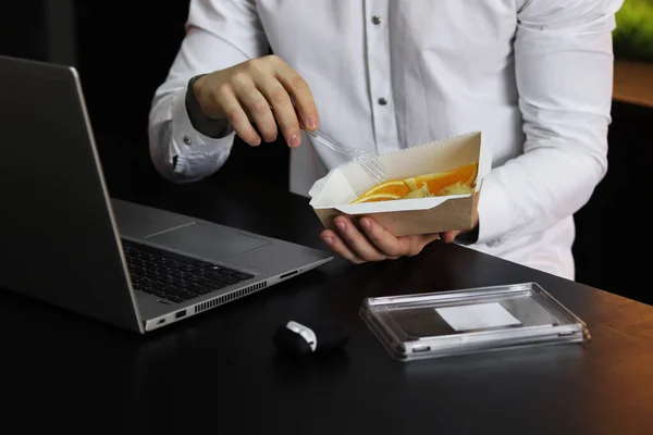 Healthy lunch at office workplace. Man eating nutrition lunch from takeaway lunch box at working table with laptop