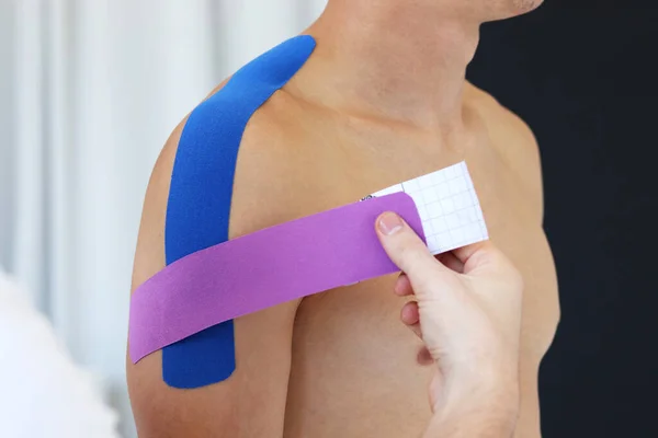 Kineziyoloji bandı. Fizyoterapist hastanın omzuna kinezyoloji bandı uyguluyor. Erkek terapist, erkek sporcunun yaralı omzunu tedavi ediyor. Travma sonrası rehabilitasyon, spor fizyoterapisi.