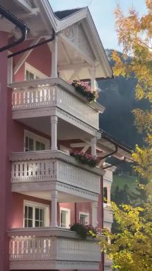 İtalya, Ortisei 'de, büyüleyici bir binanın yakın çekimi, pembe duvarları, beyaz karmaşık balkonları, ve canlı çiçek kutuları, sonbahar ağaçlarının ve dağ manzarasının zeminine kurulmuş..
