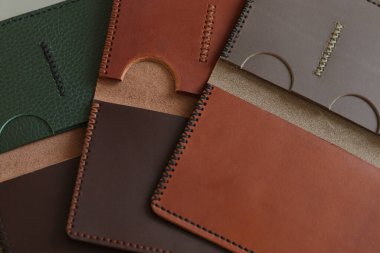 Düzgünce istiflenmiş, minimalist deri cüzdanlar koyu kahverengi ve kırmızımsı tonlarda, pürüzsüz dokuyu ve ince dikiş detaylarını sergiliyor.