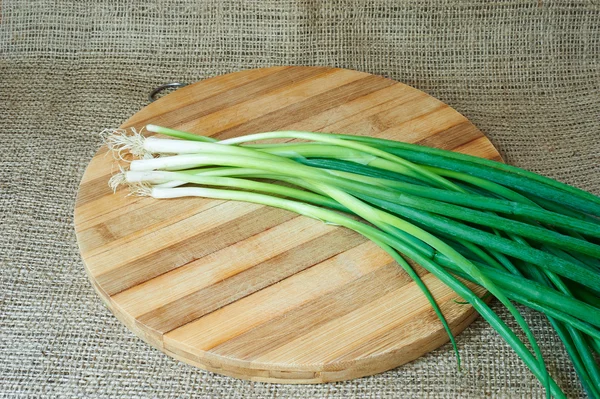 Frische grüne Zwiebeln auf einem Holztablett — Stockfoto