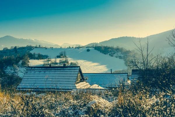 Górska wioska na mroźny słoneczny dzień w zimie. Piękny pagórkowaty krajobraz w tle. — Zdjęcie stockowe