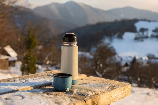 Hot tea in thermos flask on a cold winter day.Mountains in background. — Stock Photo, Image