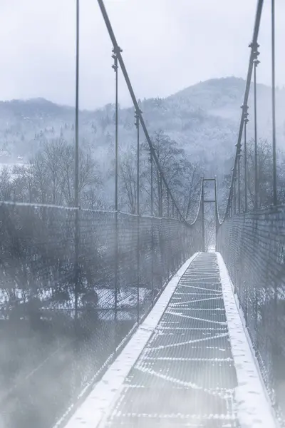 Visící most přes řeku.Hory v pozadí.Zimní obraz. — Stock fotografie
