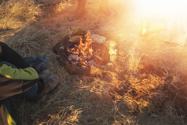 İnsanlar çayırda kamp ateşi etrafında oturuyorlar..