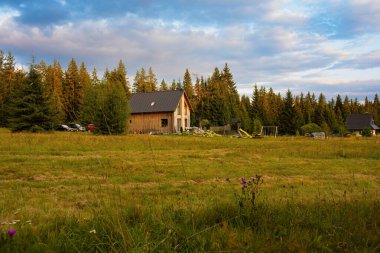 Orman ve dağlarla çevrili yeşil bir çayırda bulunan kırsal ahşap kulübe. Gün batımında dramatik bulutlu gökyüzü olan manzaralı bir yer..