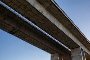 Güçlü sütunları ve berrak mavi gökyüzü olan modern beton bir köprünün alçak açılı görüntüsü. Güç, istikrar ve kentsel altyapıyı gösteren soyut mimari ve inşaat mühendisliği kavramı.