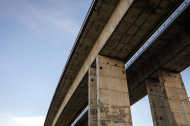 Açık mavi gökyüzünün altındaki devasa sütunlar tarafından desteklenen modern beton köprünün alçak açılı görüntüsü. Güç, istikrar, inşaat mühendisliği ve modern altyapı tasarımı sembolü.