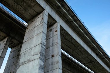 Açık mavi gökyüzünün altındaki devasa sütunlar tarafından desteklenen modern beton köprünün alçak açılı görüntüsü. Güç, istikrar, inşaat mühendisliği ve modern altyapı tasarımı sembolü.