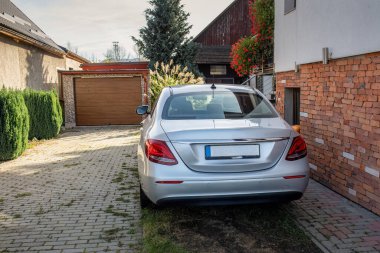 Modern gümüş limuzin kaldırımlı bir garaj yoluna park edilmiş tuğla duvarlı bir evin yanında. Günlük hayat kavramı, kişisel ulaşım, banliyöde yaşam ve ev konforu.
