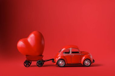 Kırmızı araba kırmızı arka planda Heart 'a hediye getiriyor. Sevdiğin kişi için sürpriz. Sevgililer Günü kavramı, düğünler, doğum günü, yeni yıl, Noel, baba ya da anne günü. Boşluğu kopyala