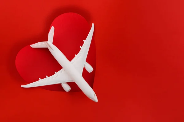 Love of travel. Valentines Day Gifts for Travel Lovers. Travel planning for Valentines day. White plane on red background heart shape. Copy space