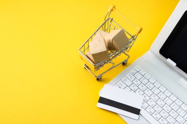 Kutulu alışveriş arabası, kredi kartı, sarı arka planda beyaz klavye bilgisayarı. Internet Online alışveriş konsepti. Boşluğu kopyala
