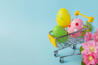 Mavi arka planda alışveriş arabasında renkli Paskalya yumurtaları. Satılık. Alışverişe. Boşluğu kopyala