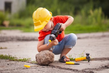Dışarıda oyuncak aletleri olan küçük bir çocuk. Çocuğu işe dahil et.