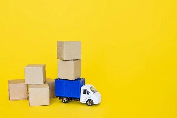 Pudełka kartonowe i niebieska ciężarówka na żółtym tle. Transport towarowy, dostawa. — Zdjęcie stockowe