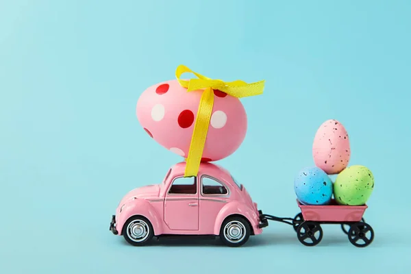 Carro e reboque entrega ovos de Páscoa no fundo azul. Compras. Preparação de férias Feliz Páscoa. Espaço de cópia — Fotografia de Stock