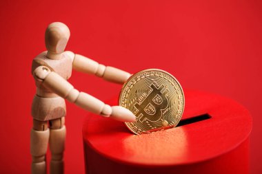 Tahta adam, kırmızı bağış kutusunun içine bitcoin sembollü altın sikke koyar. Şifreli para birimi kavramı. Seçici odak
