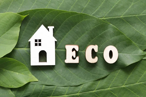 Vita trä hus, trä bokstäver Eco på gröna löv bakgrund. Miljövänligt hem koncept, hälsosam livsstil, noll avfall. — Stockfoto