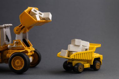 Sarı Damperli Kamyon, Kazıcı, koyu gri arka planda inşaat malzemeleri. Teslimat Malzemeleri. Kira İnşaat Malzemeleri. İnşaat endüstrisi